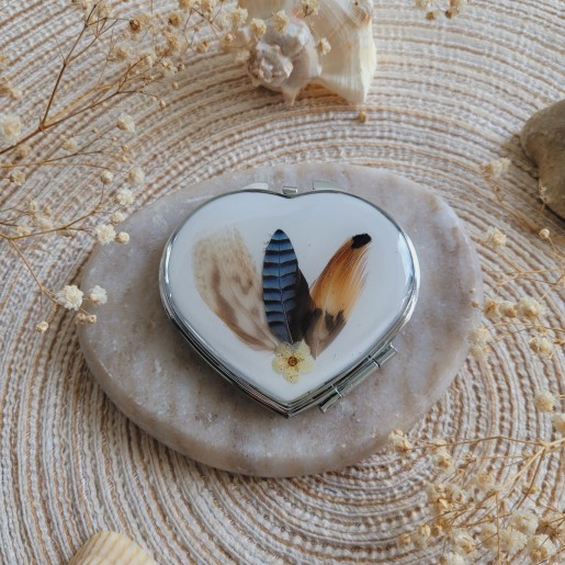 Miroir de poche coeur en métal argenté agrémenté de plumes naturelles.